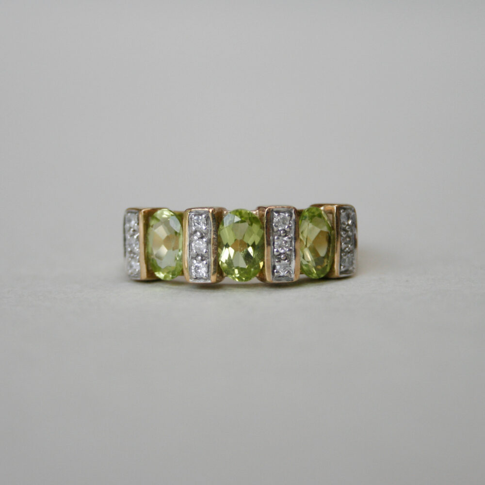 A classic three stone oval peridot and diamond band ring